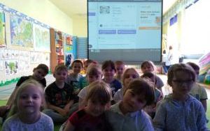 Dzieci pozują do zdjęcia na tle ekranu z wyświetlaną prezentacją multimedialną