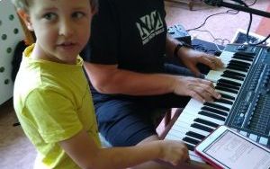 mężczyzna gra na keyboardzie z pomocą małego chłopca