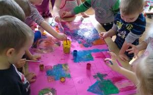 dzieci w grupie, przy stoliku, malują farbami na różowym brystolu