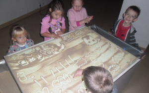 dzieci przy stole do malowania piaskiem